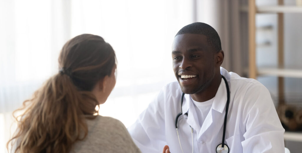Smiling,Black,Male,Doctor,Listen,Female,Patient,At,Medical,Meeting - SelectDr doctor talking to patient